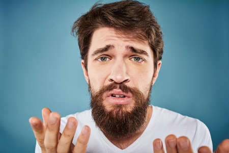 Bearded man displeased facial expression emotions close-up blue background white t-shirtの写真素材
