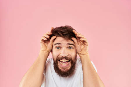 Bearded man in white t-shirt gesturing with hands facial expression close up pink background