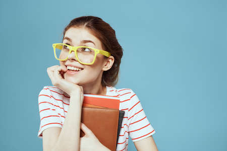 Beautiful female student with notepads and in yellow glasses on a blue background education science instituteの写真素材