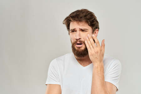 A man in a white t-shirt with a beard emotions displeased facial expression light backgroundの写真素材