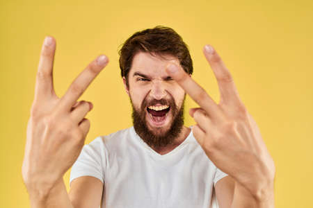 Bearded man emotions fun gesture with hands white t-shirt close-up yellow background