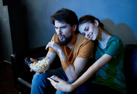 Married couple enjoying watching TV and eating popcorn on sofa.