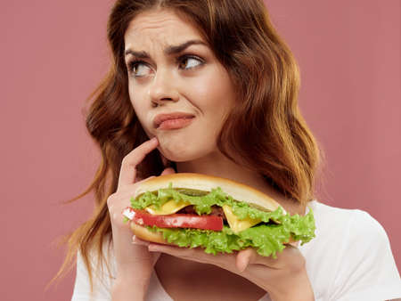 Upset woman with hamburger white tank top on pink background look