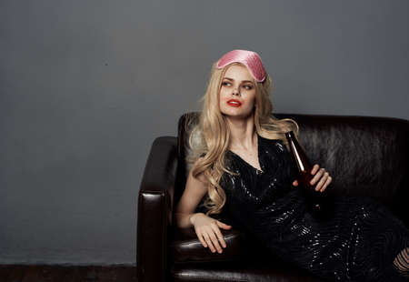 Woman on a leather couch with a bottle of beer and a sleep mask