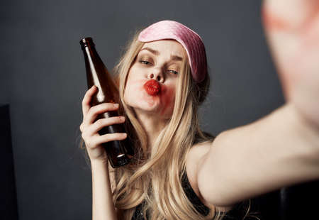 Drunk woman with a bottle of beer on a gray background gestures with her hands and bright makeup