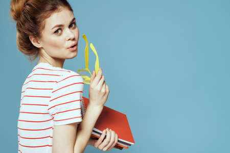 Beautiful female student with notepads and in yellow glasses on a blue background education science...