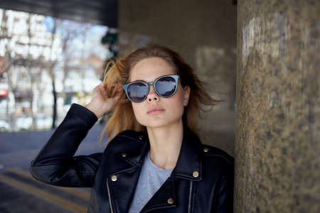 a woman stands under a bridge in the street wearing sunglasses and a leather jacketの写真素材