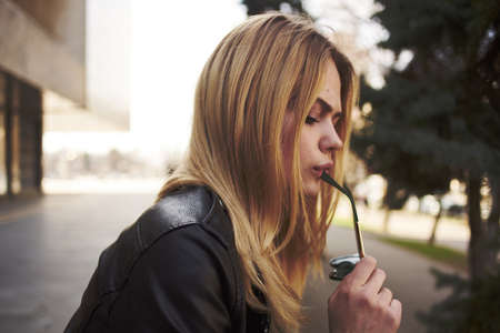 Happy blonde woman in leather jacket trendy glasses nature park street