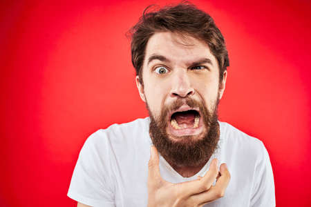 bearded man gesturing with hands white t-shirt emotions facial expression aggression red isolated backgroundの写真素材