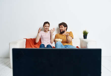 Friends man and woman sit on the couch in front of the TV indoors and a flower in a potの写真素材
