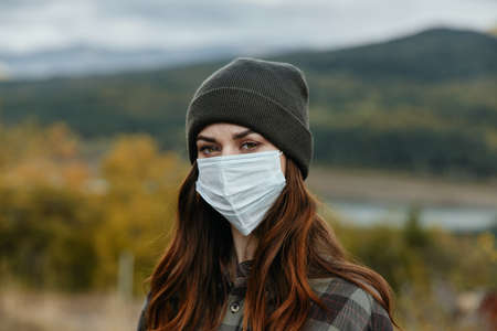 Portrait of a woman in a medical mask on a background of an autumn forest in natureの写真素材