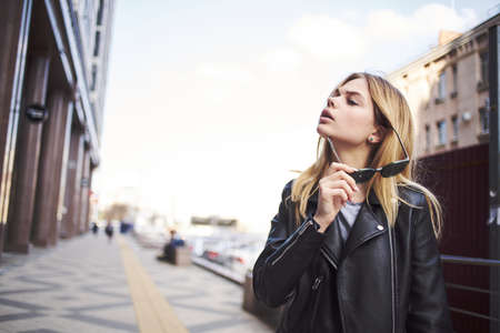 Fashionable woman wearing leather jacket outdoors near the building blonde fresh airの写真素材