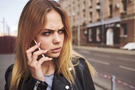 Cropped view of blonde woman with mobile phone on the street near the building
