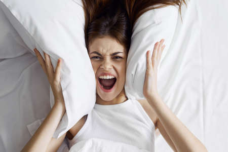 aggressive woman in bed covering her ears with pillows and shoutingの写真素材