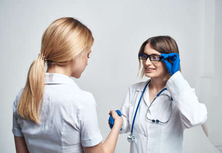 The nurse shakes hands with the patient on a light background and blue gloves with a stethoscopeの写真素材