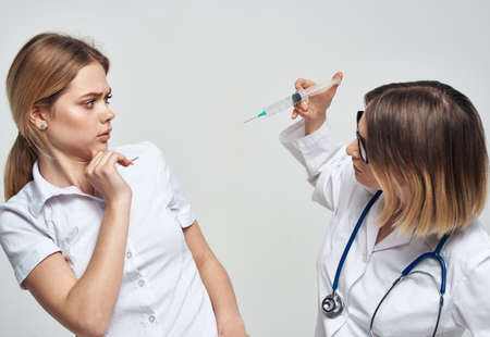 Female doctor shows the patient a syringe and a medical gown a stethoscopeの写真素材