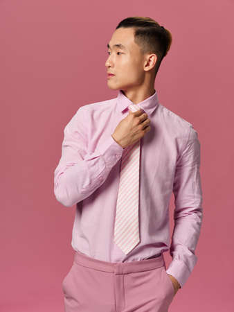 Handsome man of Asian appearance straightens his tie with a look towards pink backgroundの写真素材