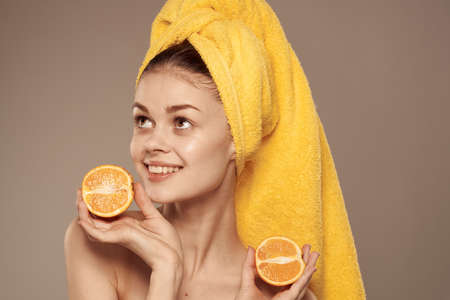 Pretty woman bared shoulders oranges in the hands of a yellow towel on her headの写真素材