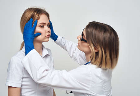 A woman doctor in a medical gown and blue gloves examines the patients faceの写真素材