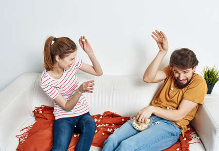 cheerful man and woman on the couch with popcorn and red plaid flower in a pot emotions