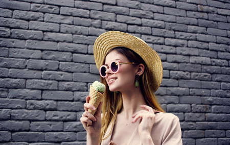 Cheerful woman with ice cream in a hat near a brick wall