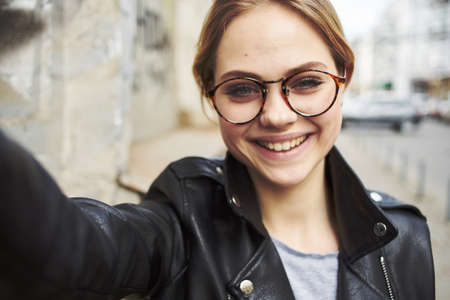 Portrait of a happy woman in glasses and in a leather jacket outdoors smiling model