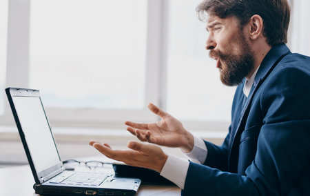 business man sitting at a table in a suit in front of a laptop emotions office managerの写真素材