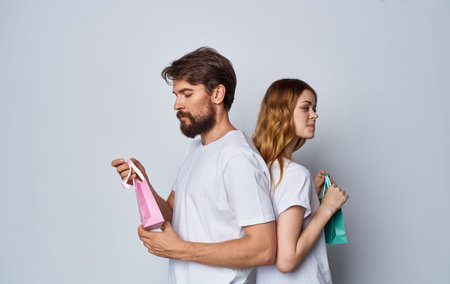 man and woman with gift bags stand back to each other on gray background