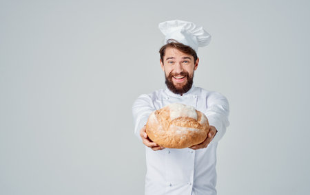 Happy cook in connected clothes holds a loaf of fresh bread in his hand