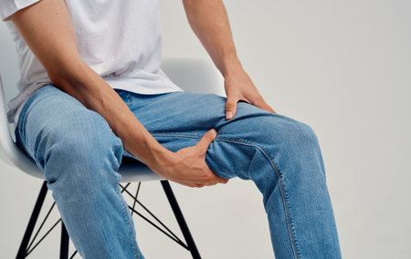 man in jeans sitting on a chair and touching his leg with his hands cropped viewの写真素材