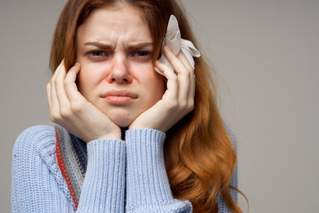 woman with a runny nose touches her head with her hands on a gray background portrait close-up