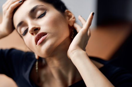 beautiful woman with closed eyes touches her face with her hands earrings makeup model evening dress
