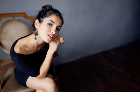 attractive brunette in black dress sits on a chair indoors and sexy appearance, earringsの写真素材