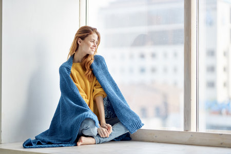pretty woman in a plaid sits on the windowsill and looks out the windowの写真素材