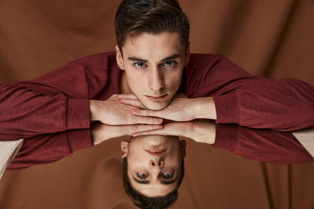 A man in a shirt is leaning against the glass with a reflection in the mirror on a brown background