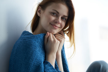 pretty woman covered with a blanket sits at home near window weekend