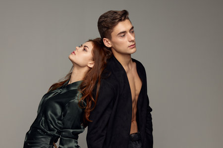 A sexy man in an unbuttoned shirt and a woman in an evening dress stand with their backs to each otherの写真素材