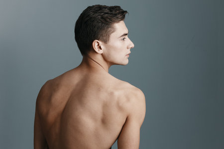 Rear view of a sexy man with a naked back looks to the side on a gray backgroundの写真素材