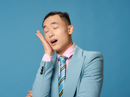 Asian man touching his face with his hand on a blue backgroundの写真素材