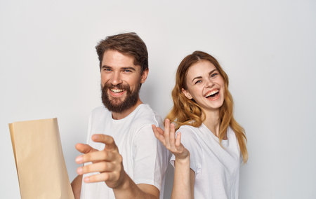 Cheerful young couple in white T-shirts package with groceries running thumb upの写真素材