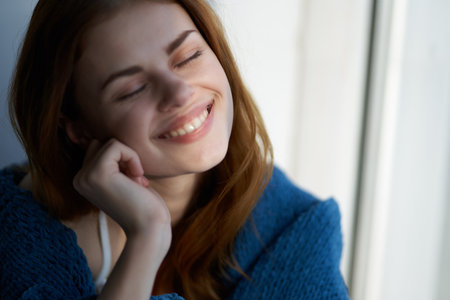 smiling woman hiding with a blanket near the window rest morning sunの写真素材