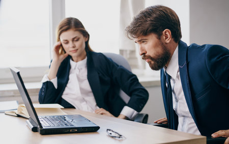 Business men and woman sit at a work table in front of laptop emotions officeの写真素材