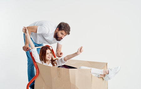 man courier looks at woman in box on cargo cart light backgroundの写真素材