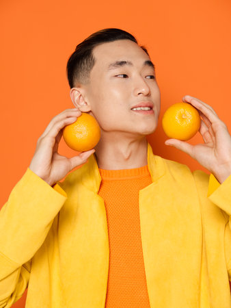 Asian man holding two orange fruits in his hands on an isolated backgroundの写真素材