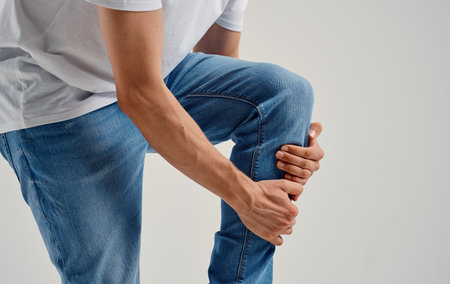 man in jeans touches his knee with his hands on a light background cropped view