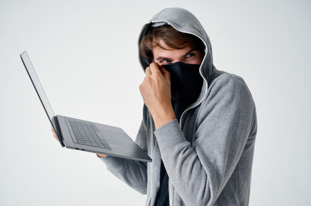 man in gray hoodie with laptop hidden mask hacking computer