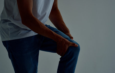 the guy touches his leg with his hands on a light background knee pain
