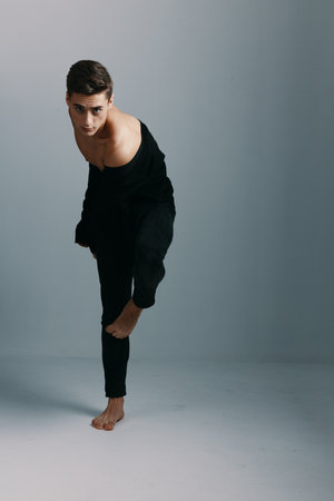 Sexy guy in a dark suit on a gray background leaned forward in full growthの写真素材