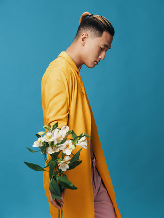 Side view of a man in a yellow coat holding a bouquet of white flowers on a blue backgroundの写真素材