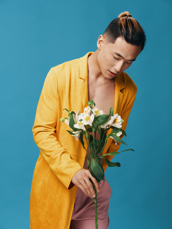Fashionable man in a yellow coat examines a bouquet of white flowers in his hands on a blue backgroundの写真素材